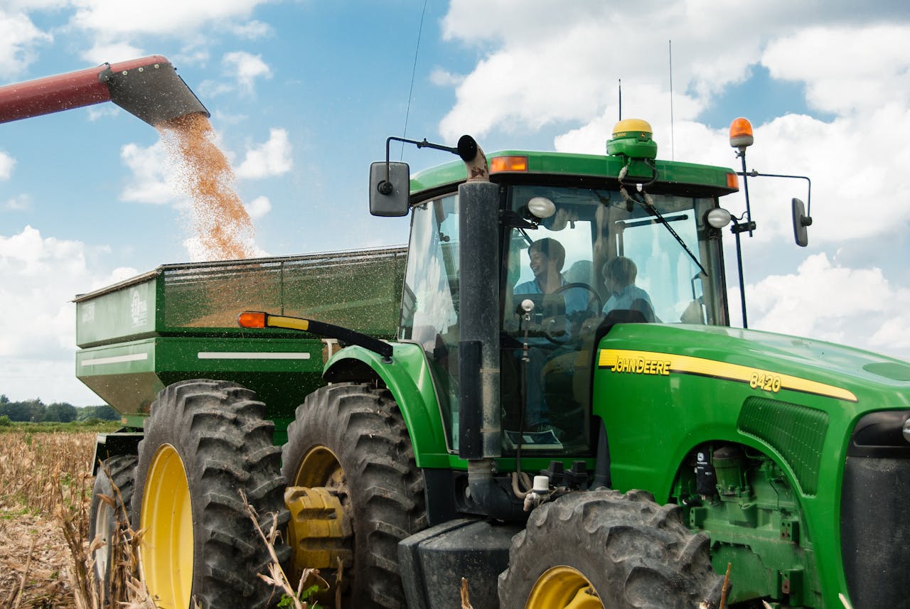 Green tractor harvesting crops in a sunny rural field, showcasing modern agriculture.